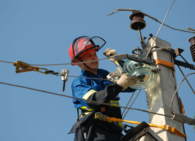 An electrician installs insulators on a pole. 